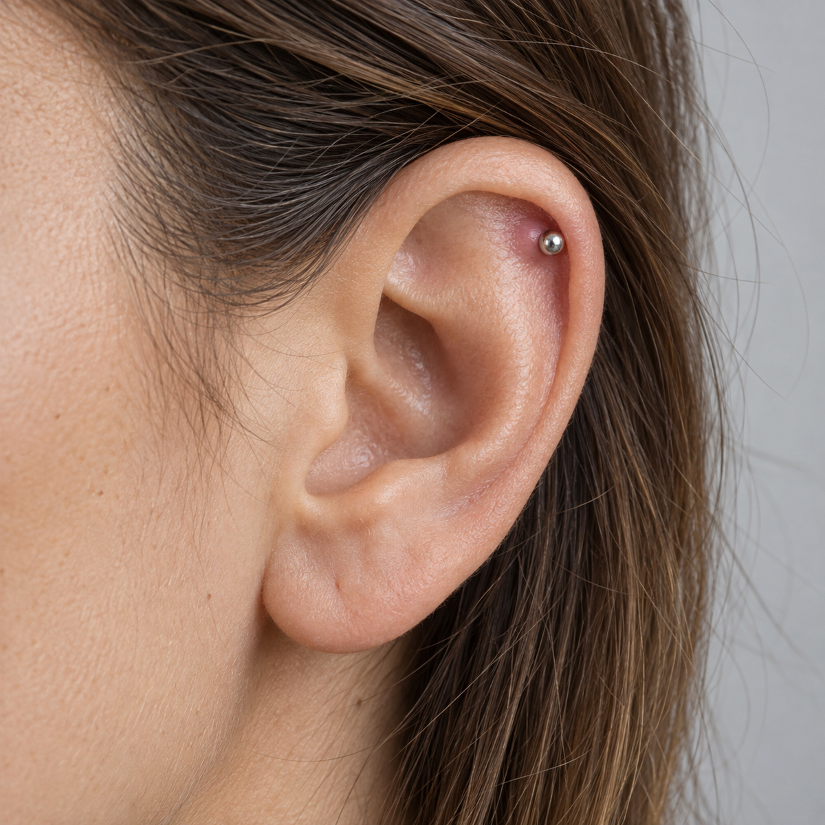 Illustrative close-up of an ear with a silver helix stud and a small raised pink area beside it.