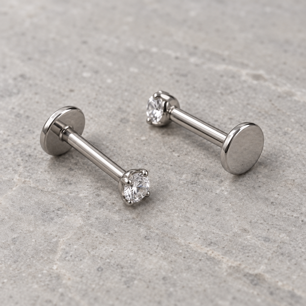 Two silver flat-back labret earrings with clear gemstone tops, showing their smooth disc backs.