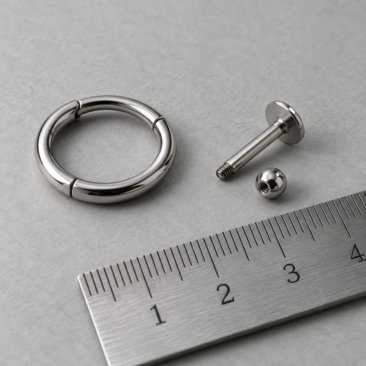 Illustrative silver ring and labret beside a ruler, showing jewellery sizing concepts.