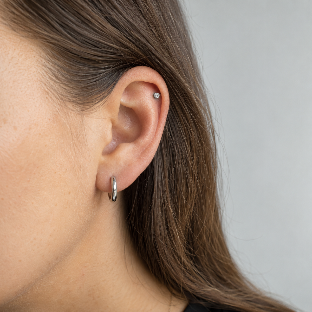 Close-up of an ear wearing a silver helix stud and lobe hoop.